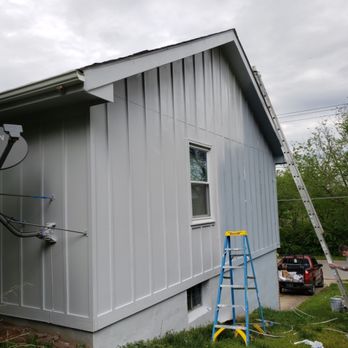 Gray board-and-batten siding freshly painted, ladder against wall
